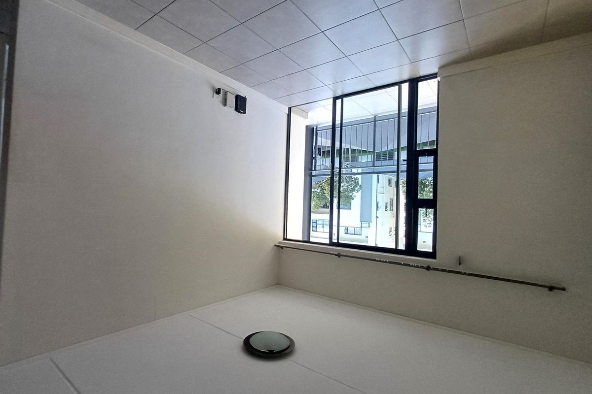 An empty bedroom featuring a tiled ceiling, large sliding window with a metal handrail, and neutral white walls.