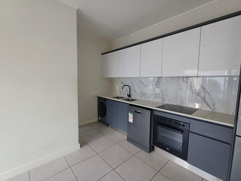 Modern kitchen featuring sleek dark grey cabinetry, white upper cabinets, marble-look splashback, integrated oven, electric hob, and tiled flooring.