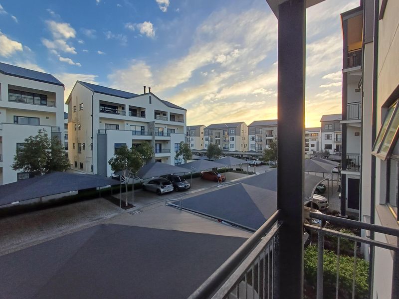 An elevated view overlooking the apartment complex grounds, featuring modern multi-story residential buildings and covered parking bays at sunset.