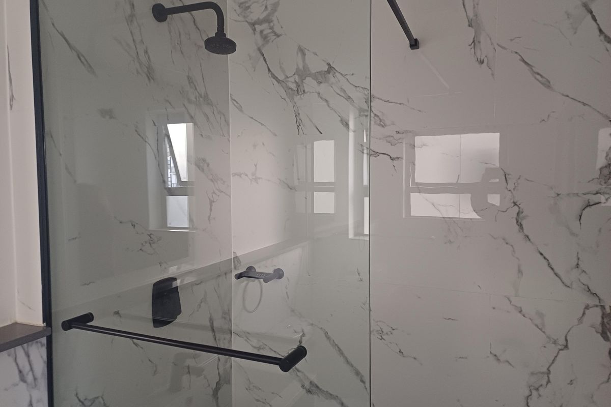 Modern bathroom shower enclosure featuring high-end marble-look wall tiles, frameless glass screen, and contemporary matte black fixtures.
