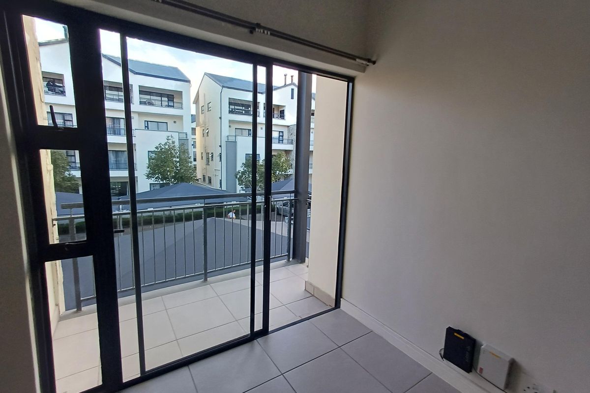 An empty living area featuring large sliding glass doors that open onto a private balcony with a metal balustrade and tiled flooring.