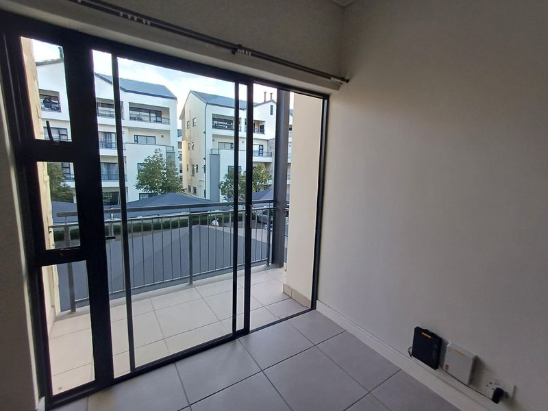 An empty living area featuring large sliding glass doors that open onto a private balcony with a metal balustrade and tiled flooring.