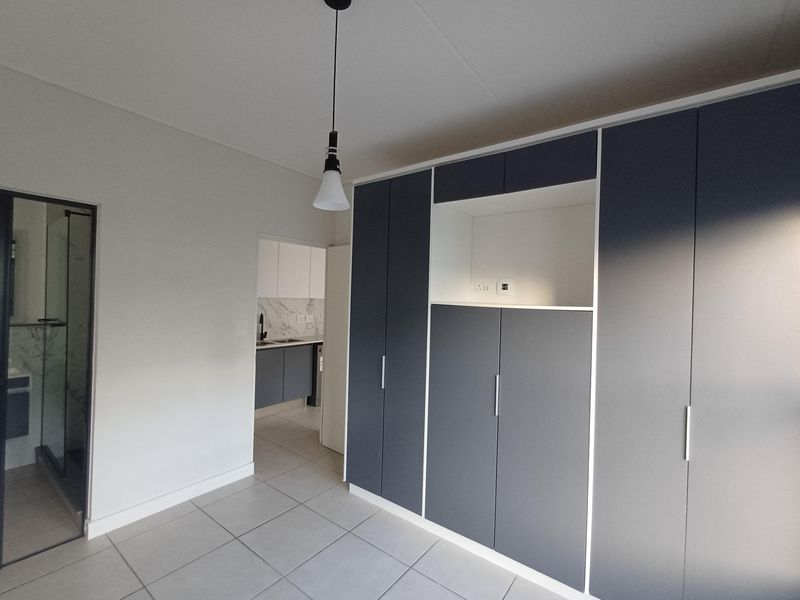 Modern bedroom featuring sleek built-in cupboards, neutral tiled flooring, and direct access to an en-suite bathroom.