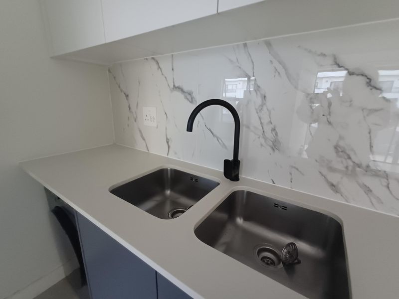 A modern laundry area featuring a double stainless steel sink, black mixer tap, and elegant marble-look splashback with stone countertops.
