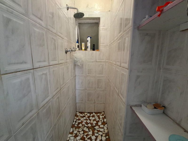 A compact shower enclosure featuring dated wall tiles, a mosaic tiled floor, and a built-in storage shelf.