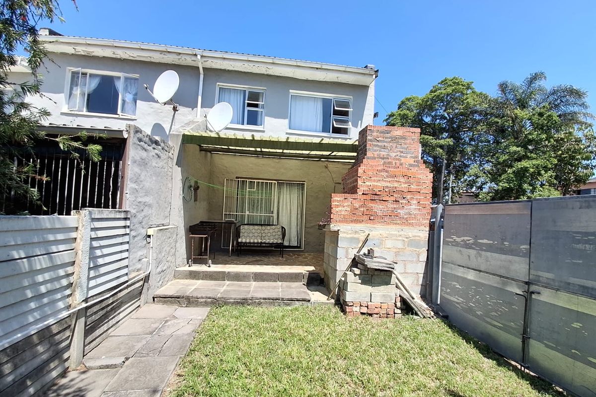 Rear exterior view of the apartment featuring a paved patio area, a brick braai structure, and a small garden space.