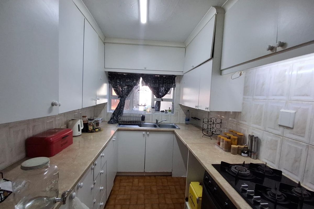 A functional galley-style kitchen featuring white built-in cabinetry, laminate countertops, a gas hob, and a double basin sink with tiled backsplash.