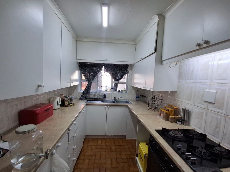 A functional galley-style kitchen featuring white built-in cabinetry, laminate countertops, a gas hob, and a double basin sink with tiled backsplash.