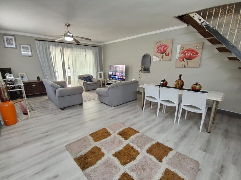 Open plan living and dining area featuring light laminate flooring, a ceiling fan, and an internal staircase with a decorative wall niche.