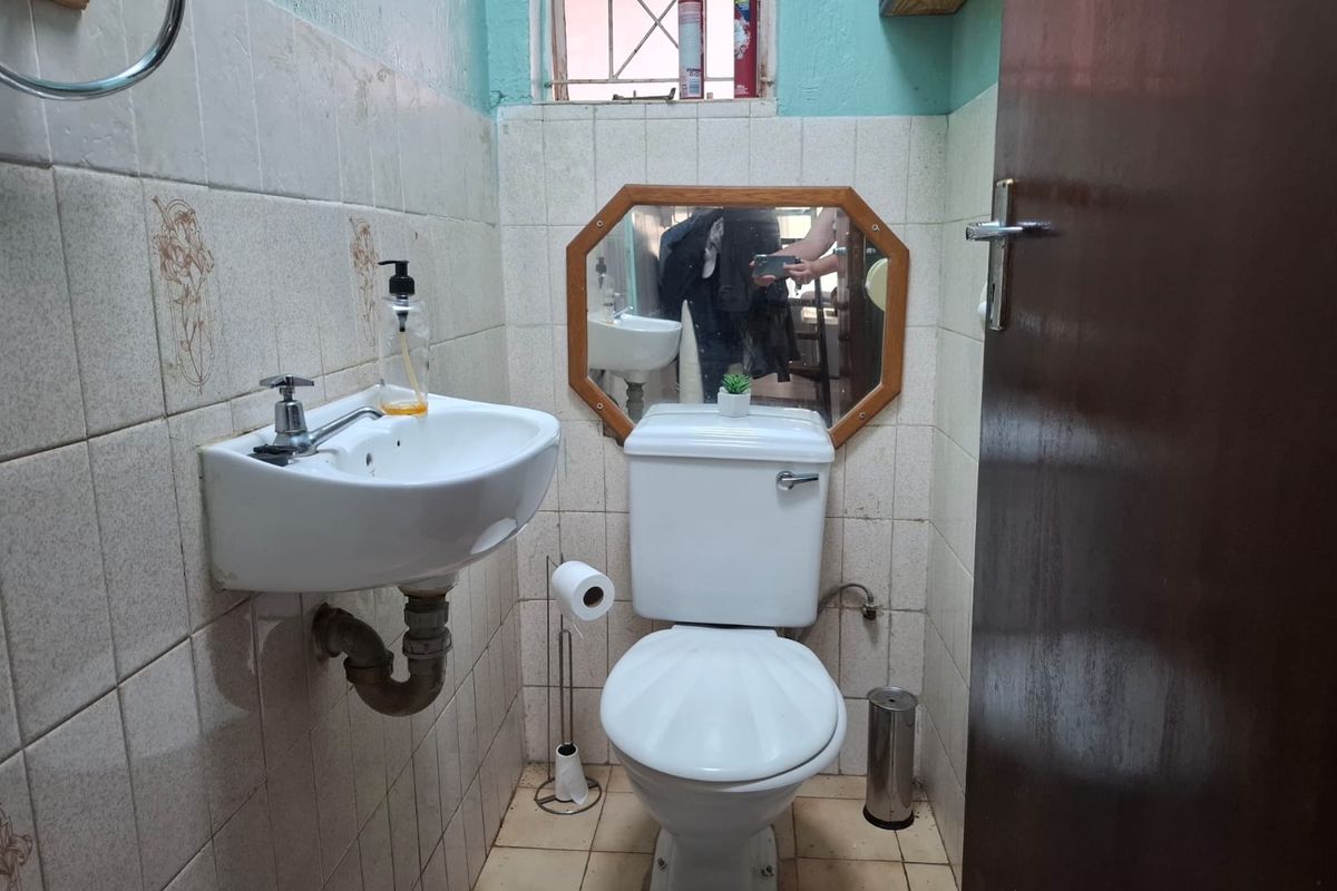 A compact guest bathroom featuring a wall-mounted basin and toilet with dated ceramic tiling and security bars on the window.