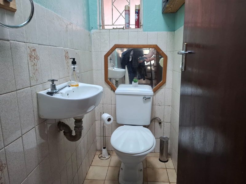 A compact guest bathroom featuring a wall-mounted basin and toilet with dated ceramic tiling and security bars on the window.
