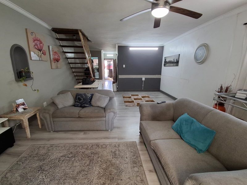 Open-plan living area featuring laminate flooring, a ceiling fan, and a staircase, with some areas requiring minor cosmetic finishing and wall repairs.