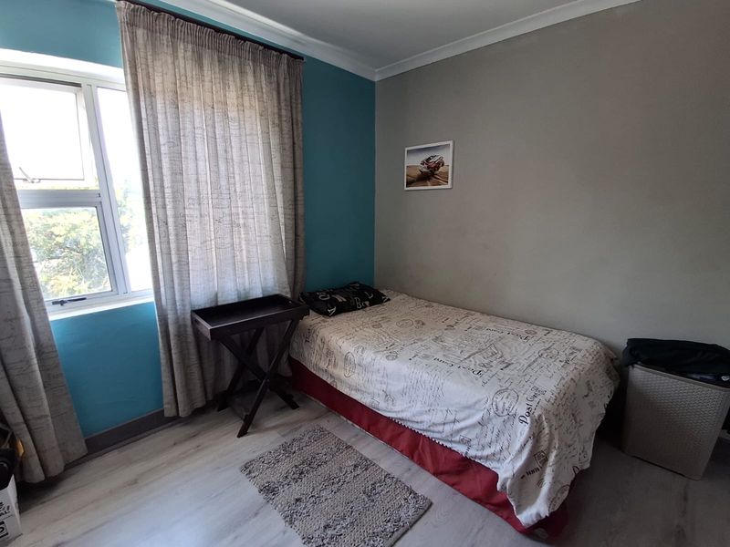 A functional bedroom featuring laminate flooring, neutral and accent wall paint, and an aluminium window frame with curtaining.