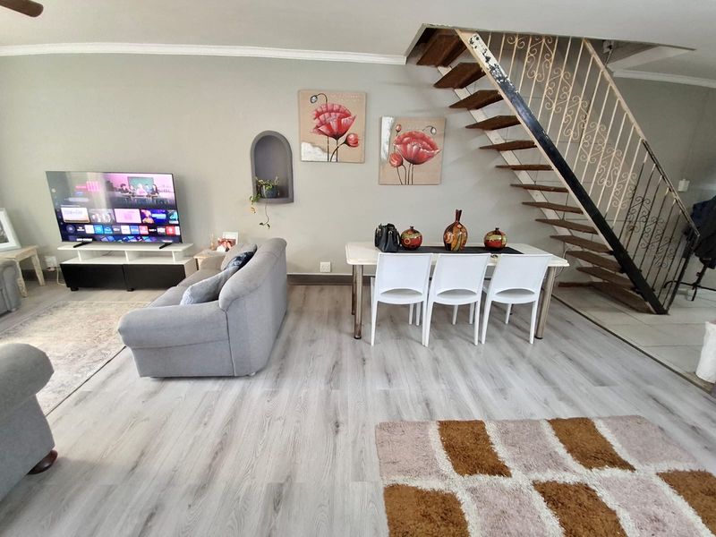 Open-plan living and dining area featuring light-toned laminate flooring, a decorative wall niche, and an open-tread staircase with a wrought iron balustrade.
