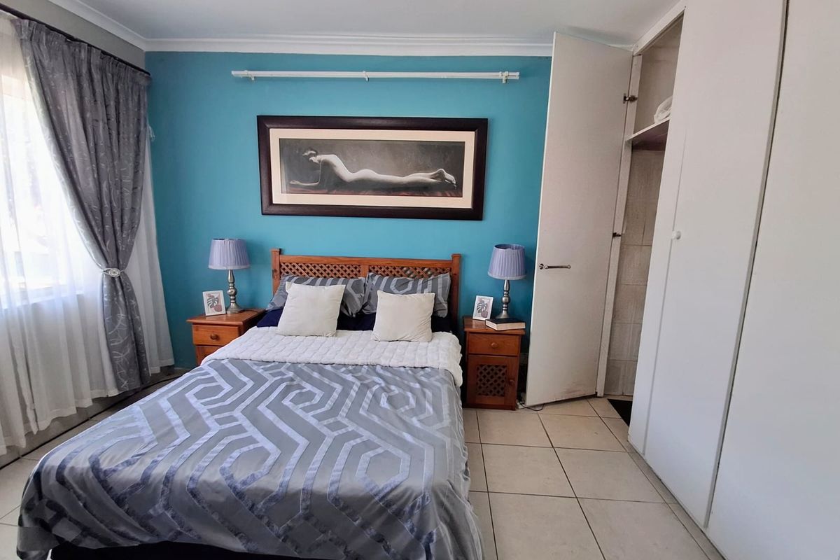 A bedroom featuring tiled flooring, built-in cupboards, and a feature wall, offering a functional space with neutral finishes.