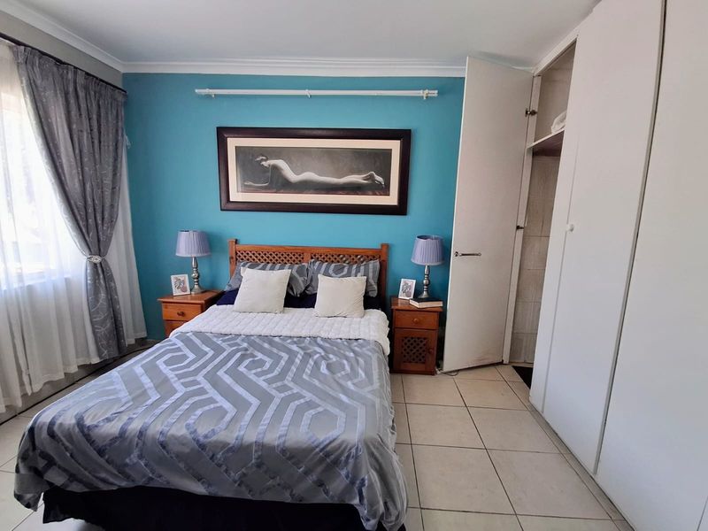 A bedroom featuring tiled flooring, built-in cupboards, and a feature wall, offering a functional space with neutral finishes.