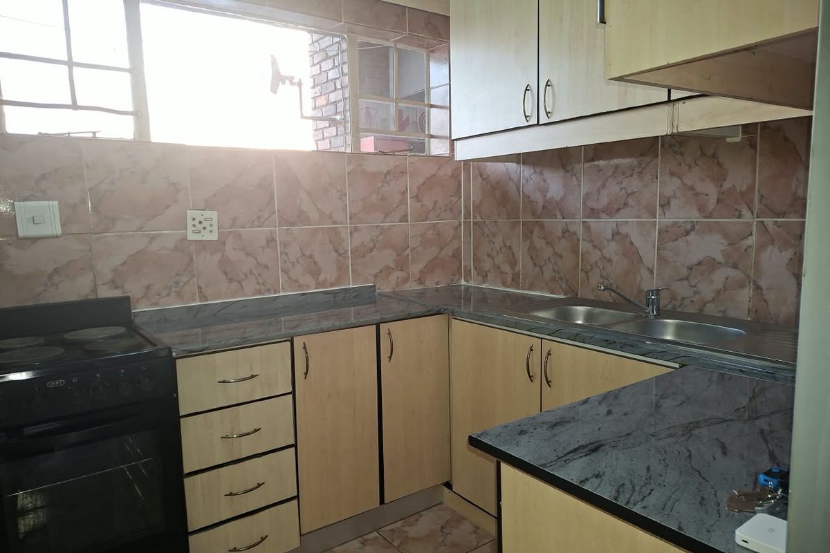 A functional kitchen featuring light wood-finish cabinetry, dark laminate countertops, a double stainless steel sink, and a freestanding stove with tiled splashbacks.