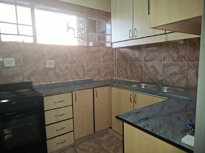 A functional kitchen featuring light wood-finish cabinetry, dark laminate countertops, a double stainless steel sink, and a freestanding stove with tiled splashbacks.