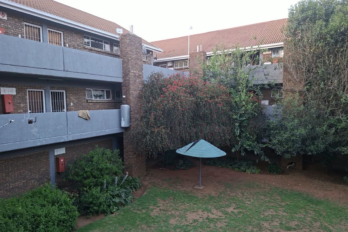 View of the rear exterior of the apartment complex, featuring brick facade, communal garden area, and balcony access.
