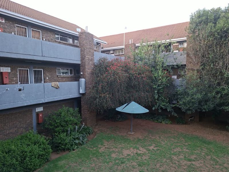 View of the rear exterior of the apartment complex, featuring brick facade, communal garden area, and balcony access.