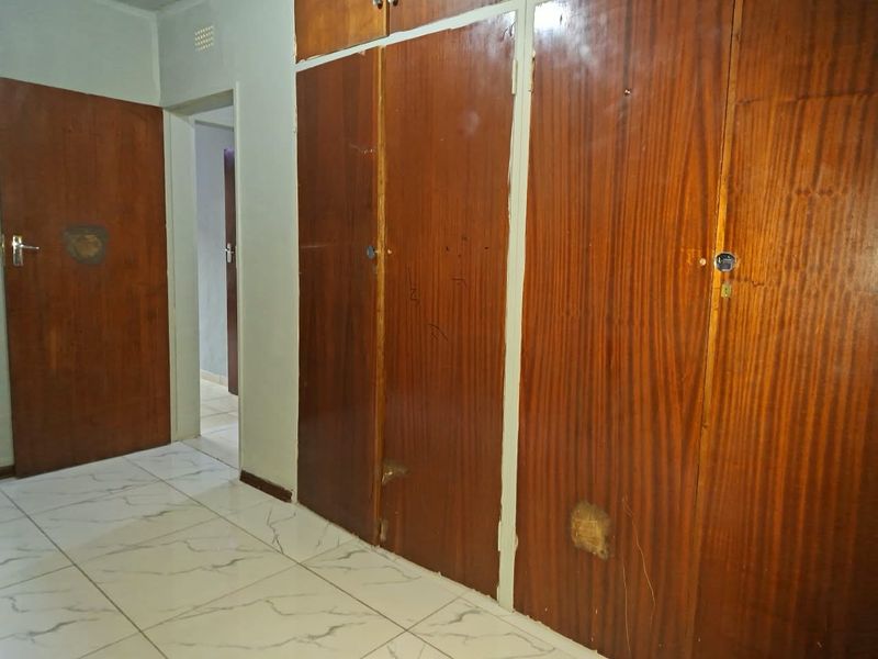 A bedroom featuring built-in wooden cupboards and tiled flooring, showing signs of wear and dated finishes.