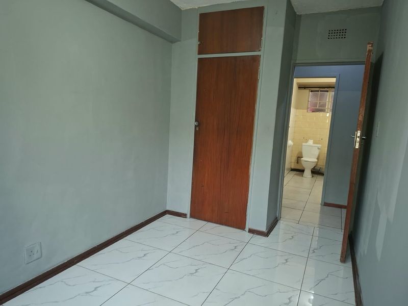 An empty bedroom featuring tiled flooring and a built-in wooden cupboard, with an adjacent view into a bathroom area.