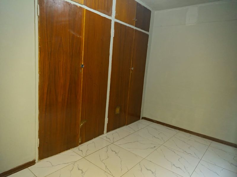 An empty bedroom featuring white marble-look floor tiles and dated wooden built-in cupboards.