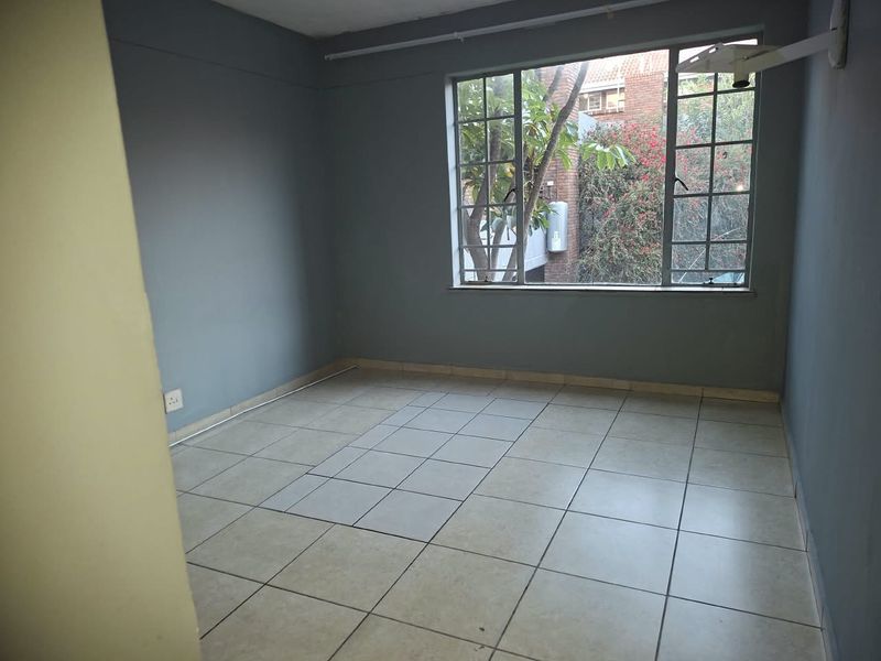 An empty bedroom featuring tiled flooring and a large steel-framed window, providing a blank canvas for potential interior design updates.