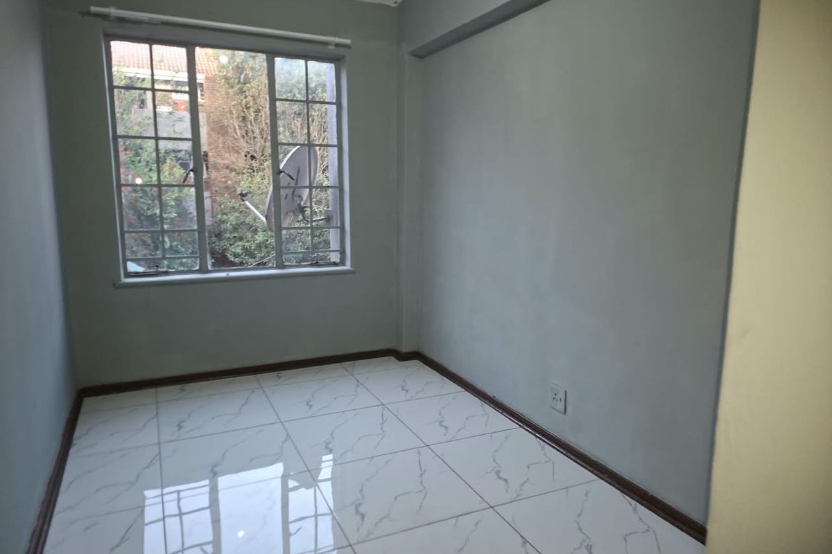 A bright, empty bedroom featuring modern white marble-look floor tiles and neutral grey walls, offering a clean and versatile space.