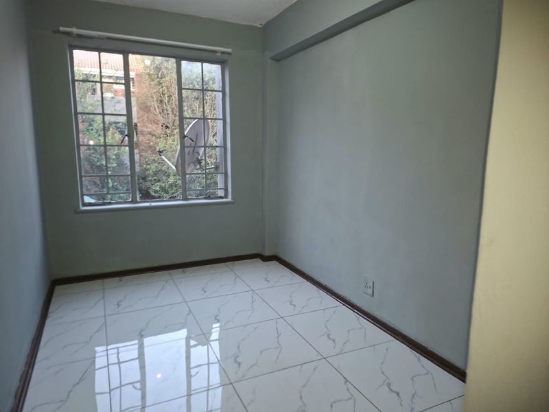 A bright, empty bedroom featuring modern white marble-look floor tiles and neutral grey walls, offering a clean and versatile space.