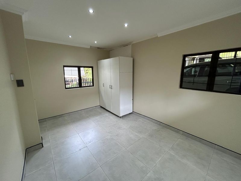 A clean, empty bedroom featuring neutral tiled flooring, recessed downlighting, and security bars on the windows, offering a versatile space ready for personalization.