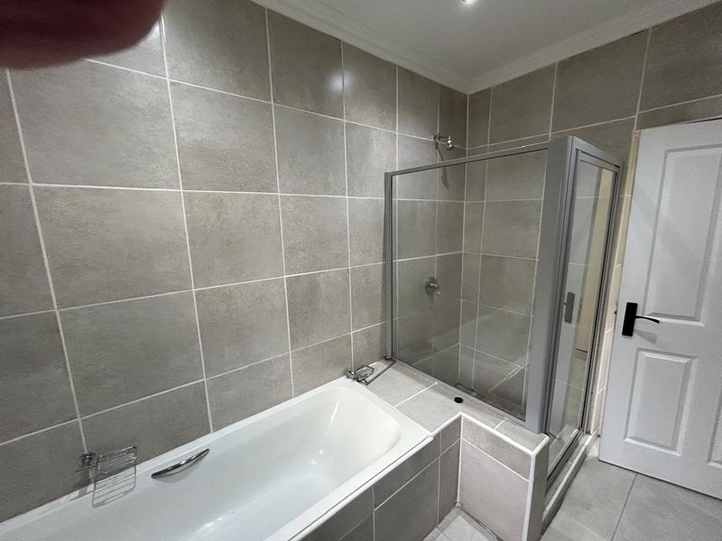 A modern bathroom featuring a built-in bathtub and a separate glass-enclosed shower with neutral wall and floor tiling.