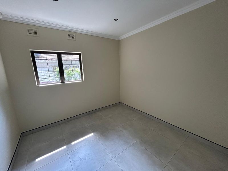 A clean, empty bedroom featuring neutral tiled flooring, recessed downlighting, and security bars on the window, providing a blank canvas for personalization.