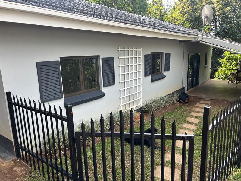 Rear view of the cottage featuring a covered patio, stone paver walkway, and secure metal fencing surrounding the garden area.