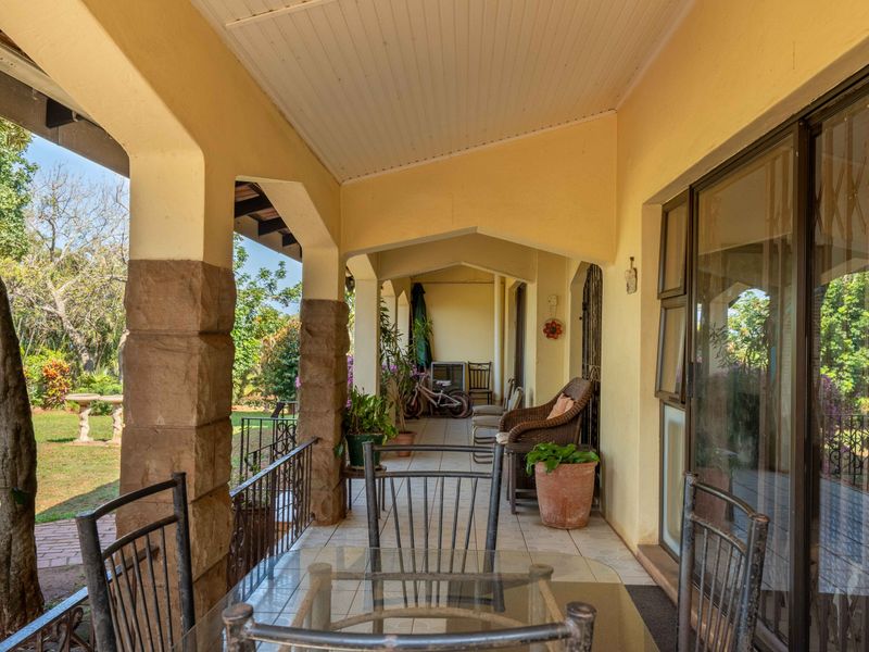 A covered patio featuring stone-clad pillars, tiled flooring, and sliding glass doors, offering a view of the garden.
