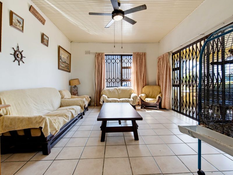 A living room featuring tiled flooring, a ceiling fan, and secure access to the exterior via a metal security gate.