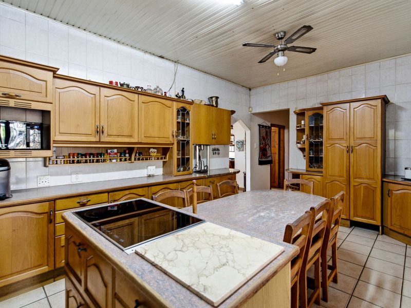 Spacious kitchen featuring extensive wooden cabinetry, a central island with an integrated induction hob, tiled splashbacks, and durable tiled flooring.