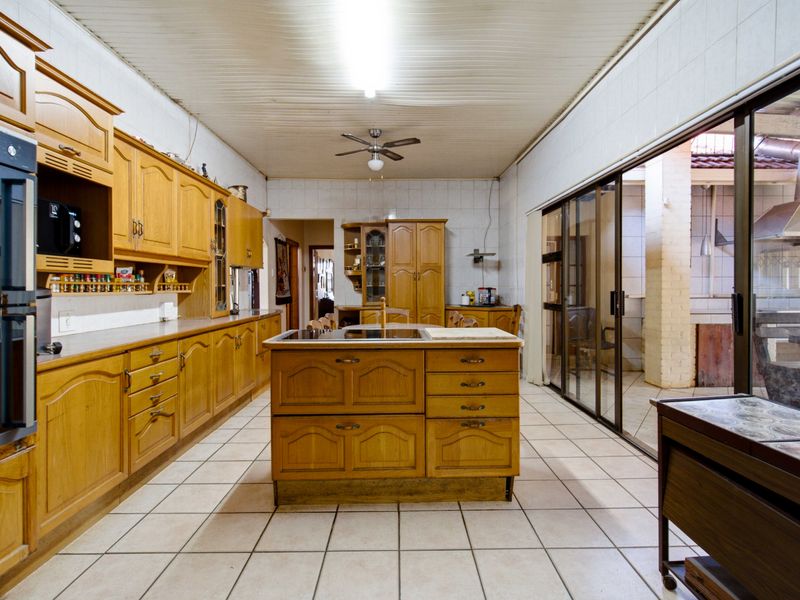 Spacious kitchen featuring extensive wooden cabinetry, a central island, built-in oven, and direct access to an outdoor patio area through sliding glass doors.