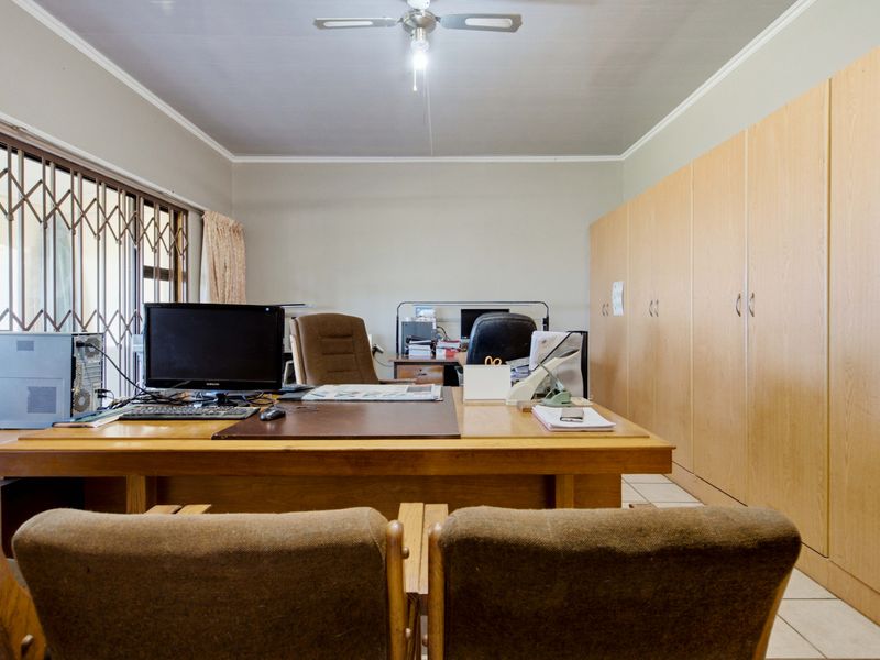 A functional home office featuring extensive built-in cabinetry, tiled flooring, and a ceiling fan, with access to the exterior via a sliding security gate.