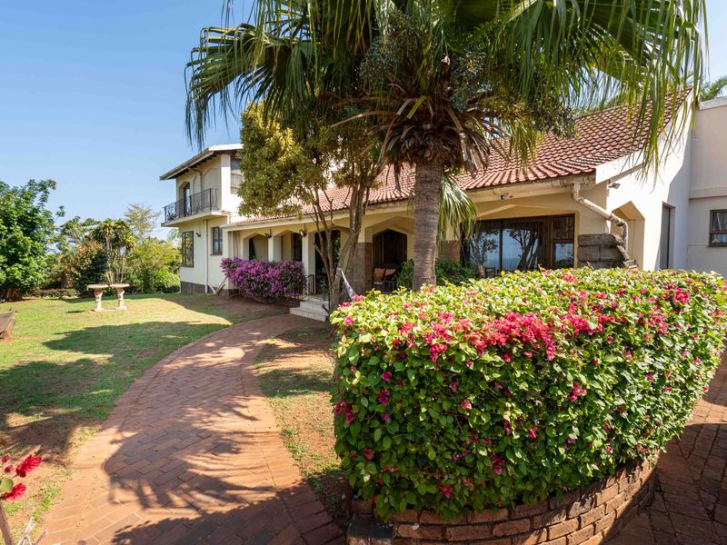A well-maintained front exterior view of the house featuring a brick paved path, established garden, and a balcony overlooking the property.