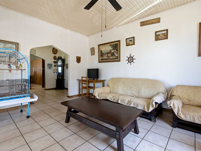 Spacious living room featuring tiled flooring, a ceiling fan, and a distinctive tongue and groove ceiling, leading through an arched doorway to adjacent areas.