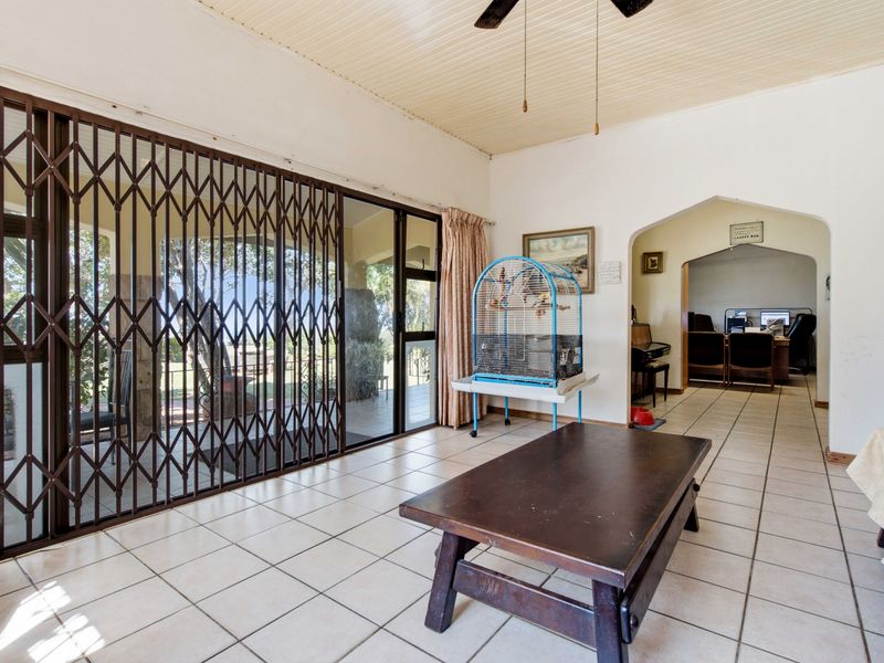 Spacious living area featuring tiled flooring, a ceiling fan, and large sliding glass doors with security gates leading to the outdoor patio.