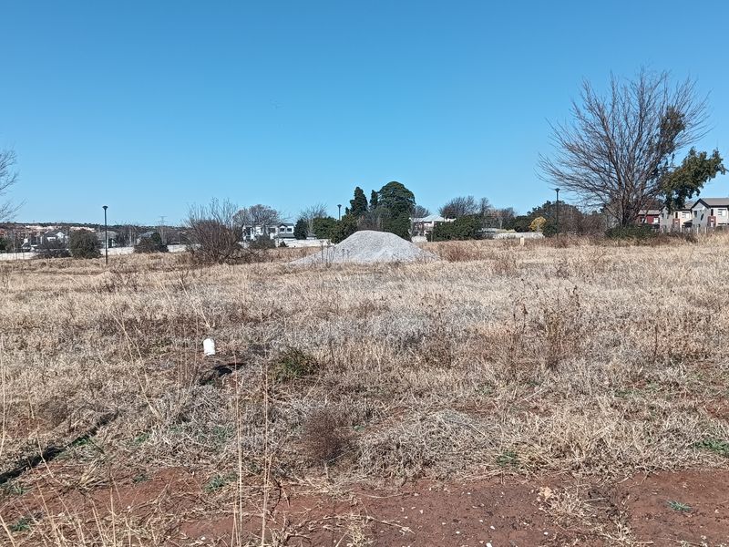 A vacant residential plot of land featuring dry grass and boundary markers, ready for development in a suburban neighborhood.