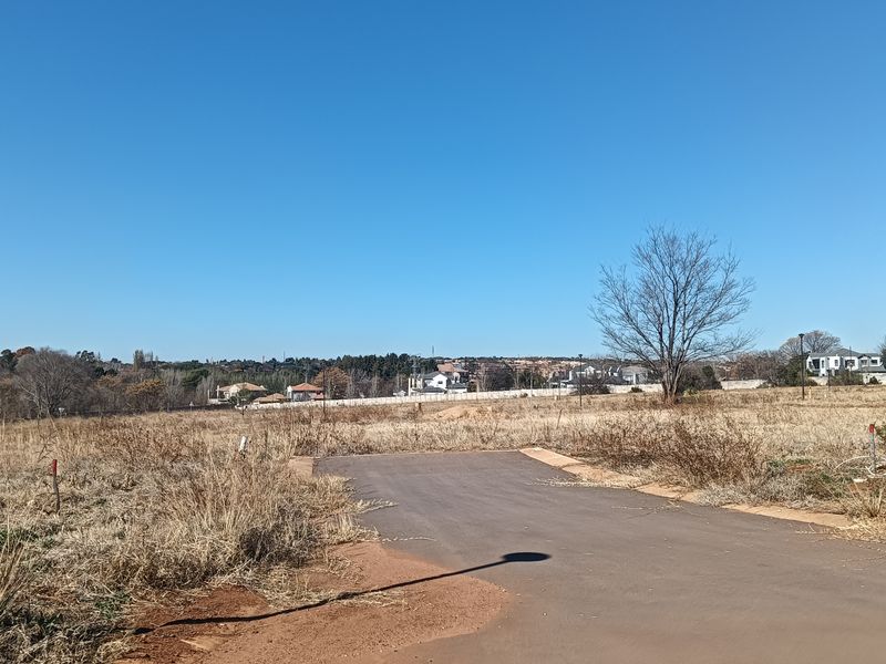 A vacant residential plot featuring a paved driveway entrance and open landscape, ready for development in a quiet neighborhood setting.
