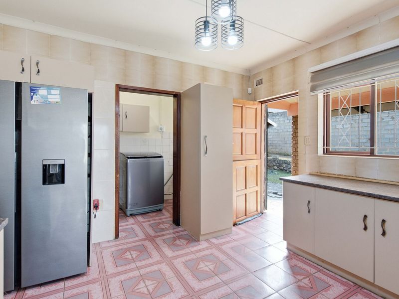 Functional kitchen featuring built-in cabinetry, tiled surfaces, and direct access to an adjacent laundry area and exterior entrance.