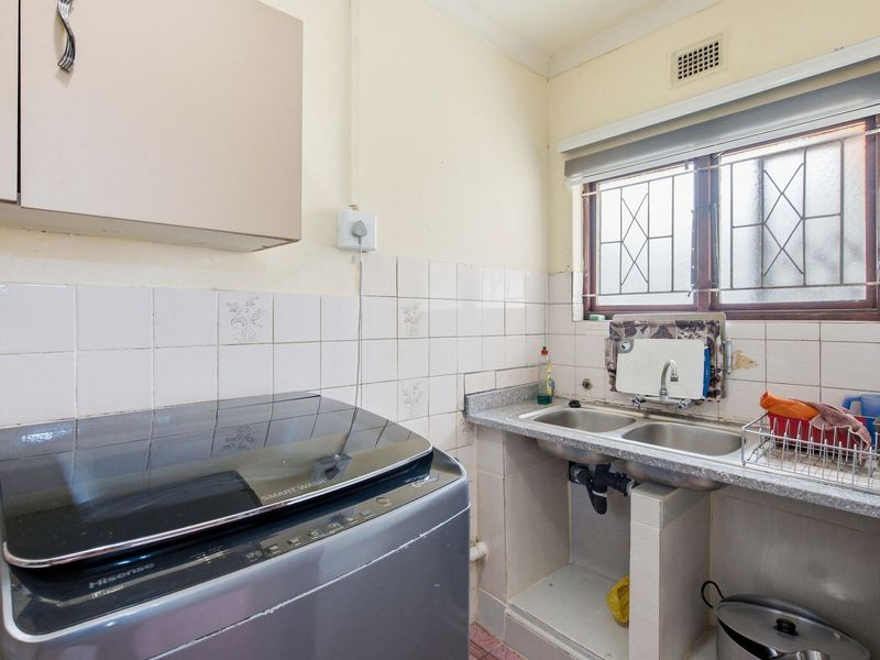Functional laundry area featuring a double stainless steel sink, tiled splashback, and built-in cabinetry with security bars on the window.