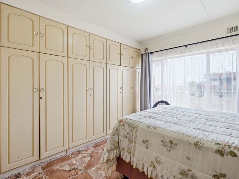 A bedroom featuring extensive built-in cabinetry, tiled flooring, and large windows with security bars, offering a functional space with potential for modern updates.
