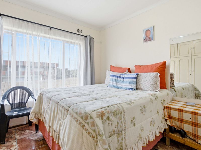 A bedroom featuring built-in cupboards, tiled flooring, and a large window with a security gate, offering natural light.