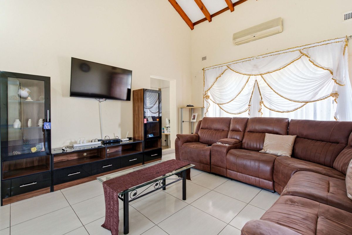 Spacious living room featuring high vaulted ceilings with exposed timber rafters, tiled flooring, and a wall-mounted air conditioning unit.