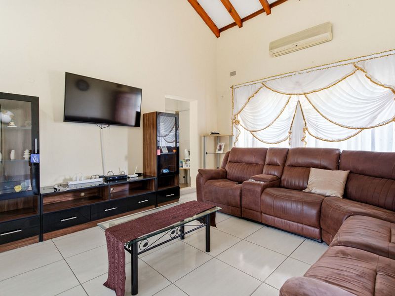 Spacious living room featuring high vaulted ceilings with exposed timber rafters, tiled flooring, and a wall-mounted air conditioning unit.